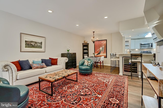 living room featuring wine cooler, an inviting chandelier, and light wood-type flooring