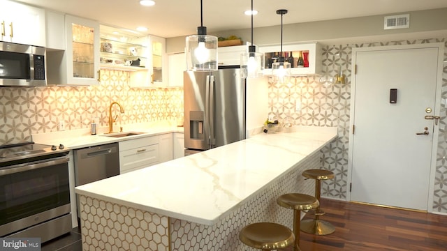 kitchen featuring a breakfast bar area, hanging light fixtures, stainless steel appliances, light stone counters, and white cabinets