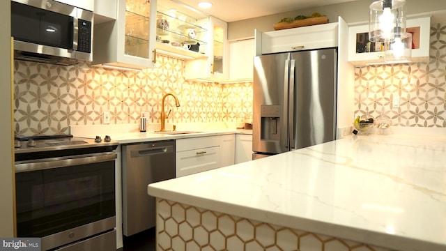 kitchen with hanging light fixtures, sink, white cabinetry, appliances with stainless steel finishes, and light stone counters