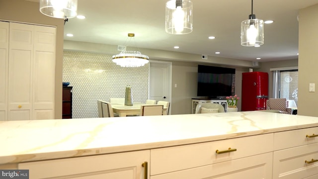 kitchen with light stone countertops, white cabinetry, and hanging light fixtures