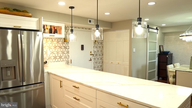 kitchen with light stone countertops, a barn door, decorative light fixtures, white cabinets, and stainless steel fridge with ice dispenser