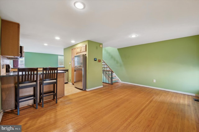 kitchen with a breakfast bar area, stainless steel refrigerator, light hardwood / wood-style flooring, and kitchen peninsula