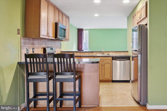 kitchen featuring a breakfast bar, sink, light wood-type flooring, kitchen peninsula, and stainless steel appliances