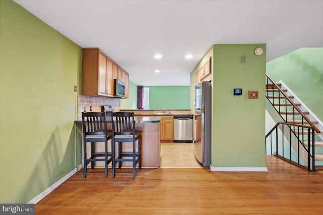 kitchen featuring kitchen peninsula, light wood-type flooring, a breakfast bar, stainless steel appliances, and sink