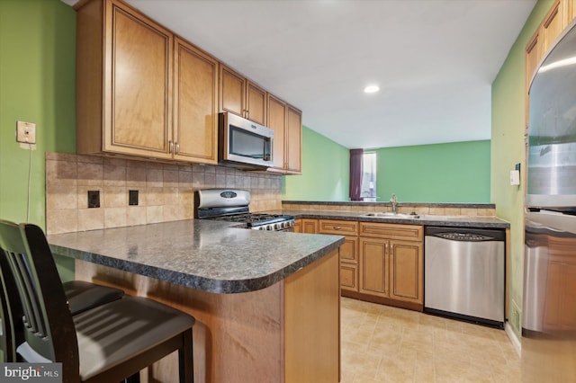 kitchen with a breakfast bar, sink, decorative backsplash, appliances with stainless steel finishes, and kitchen peninsula