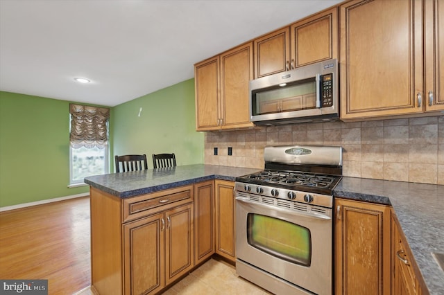 kitchen with kitchen peninsula, appliances with stainless steel finishes, decorative backsplash, and light hardwood / wood-style flooring