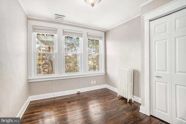 empty room with dark wood-type flooring, radiator, and crown molding