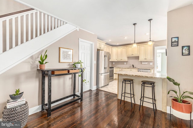 kitchen with light stone counters, appliances with stainless steel finishes, hardwood / wood-style flooring, a kitchen breakfast bar, and cream cabinetry