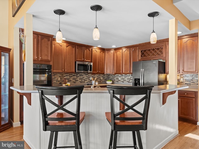 kitchen with stainless steel appliances, pendant lighting, a breakfast bar, and light wood-type flooring