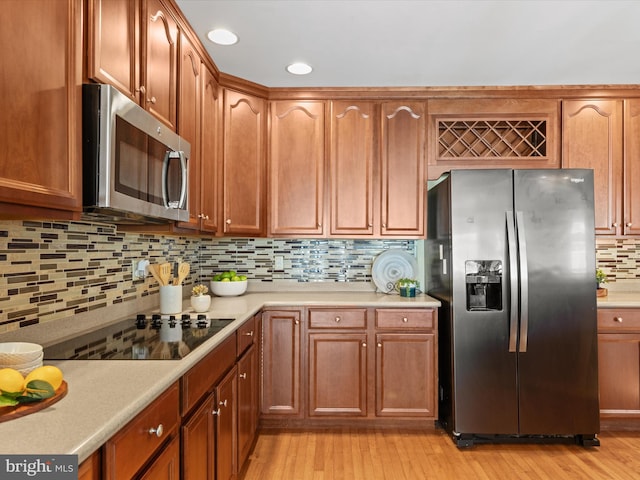 kitchen with appliances with stainless steel finishes, light hardwood / wood-style floors, and tasteful backsplash