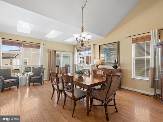 dining room with vaulted ceiling with skylight, light hardwood / wood-style flooring, and a notable chandelier