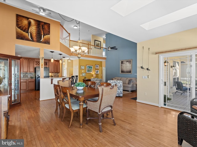 dining room with a towering ceiling, light hardwood / wood-style floors, a skylight, and ceiling fan with notable chandelier