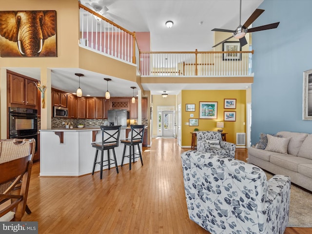 living room featuring light wood-type flooring, ceiling fan, and a high ceiling