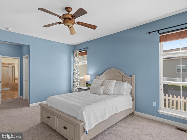 carpeted bedroom featuring multiple windows, ceiling fan, and ensuite bathroom