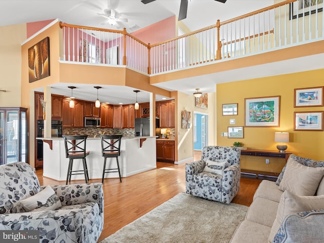 living room featuring a towering ceiling, ceiling fan, and light hardwood / wood-style flooring