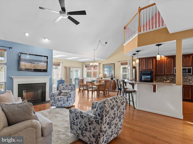 living room with ceiling fan with notable chandelier, light hardwood / wood-style flooring, and lofted ceiling