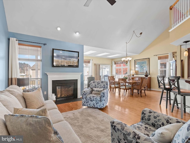 living room featuring ceiling fan with notable chandelier, light wood-type flooring, and lofted ceiling