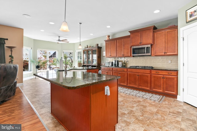 kitchen featuring gas stovetop, a kitchen island with sink, dark stone countertops, sink, and decorative light fixtures