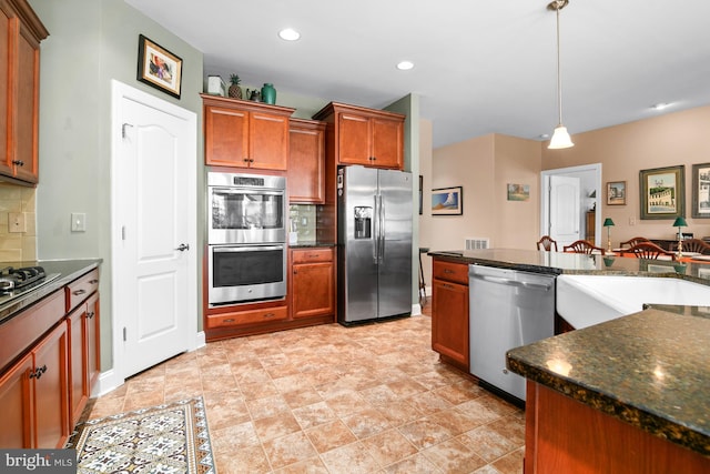 kitchen with pendant lighting, decorative backsplash, stainless steel appliances, and dark stone countertops