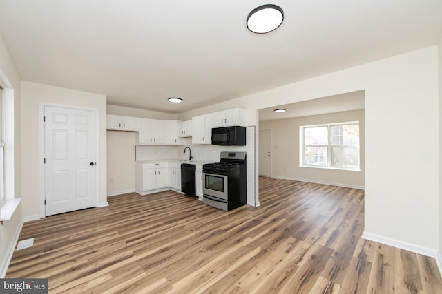 kitchen with hardwood / wood-style flooring, white cabinetry, sink, black appliances, and backsplash