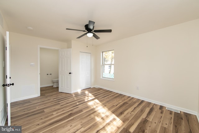 unfurnished bedroom featuring hardwood / wood-style floors, connected bathroom, ceiling fan, and a closet