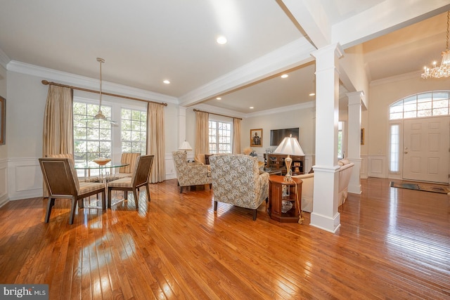 living room featuring a healthy amount of sunlight, ornamental molding, a notable chandelier, decorative columns, and light wood-type flooring