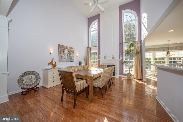 dining area with a towering ceiling, wood-type flooring, and ceiling fan with notable chandelier