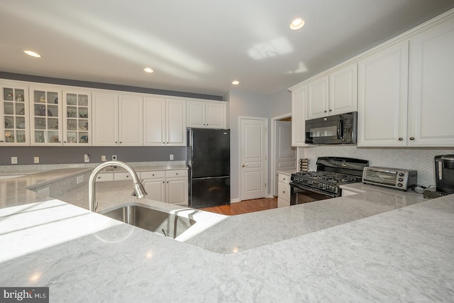 kitchen with white cabinets, sink, light stone countertops, and black appliances