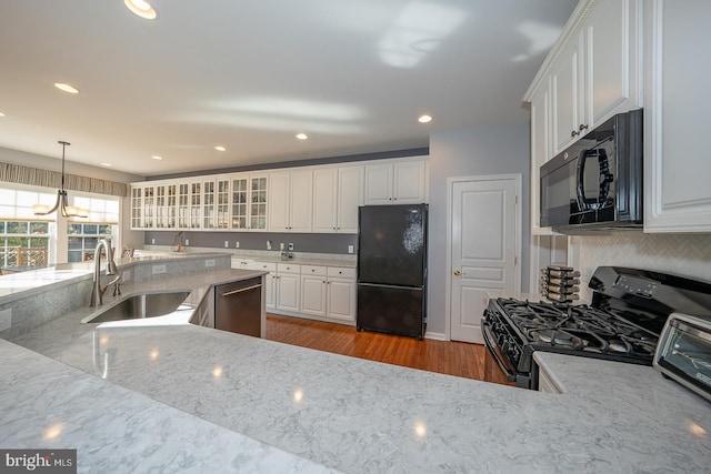 kitchen with sink, black appliances, hardwood / wood-style flooring, white cabinets, and hanging light fixtures