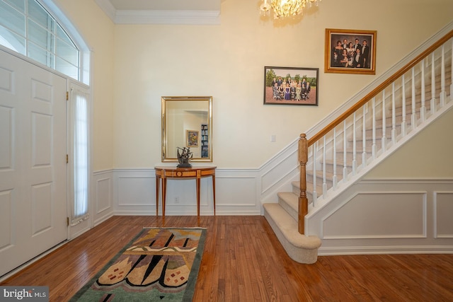 entryway with hardwood / wood-style floors, ornamental molding, and an inviting chandelier