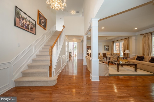 foyer entrance with hardwood / wood-style floors, decorative columns, an inviting chandelier, and crown molding