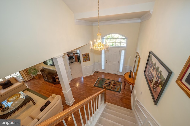 entryway featuring an inviting chandelier, decorative columns, crown molding, a towering ceiling, and wood-type flooring