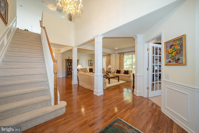 foyer entrance featuring decorative columns, wood-type flooring, a chandelier, and ornamental molding