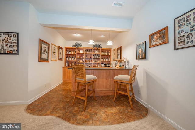 bar with hanging light fixtures and dark colored carpet