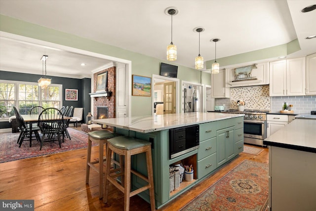 kitchen featuring a brick fireplace, a center island, light hardwood / wood-style flooring, white cabinetry, and appliances with stainless steel finishes