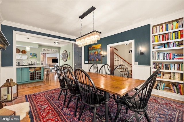 dining area with ornamental molding, built in shelves, a notable chandelier, and hardwood / wood-style flooring