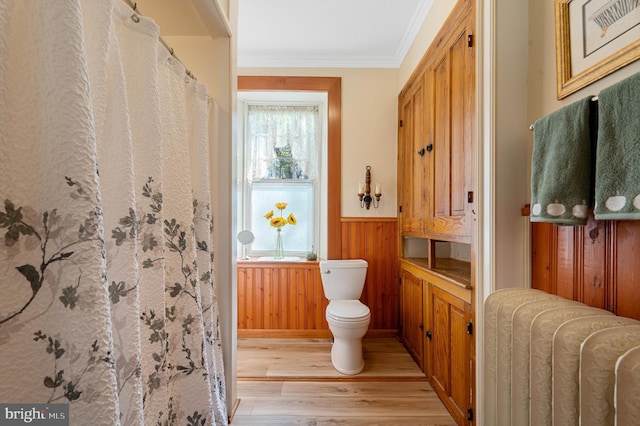 bathroom featuring toilet, ornamental molding, wooden walls, radiator, and hardwood / wood-style floors