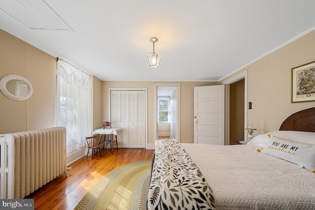 bedroom with hardwood / wood-style flooring, crown molding, radiator heating unit, and a closet