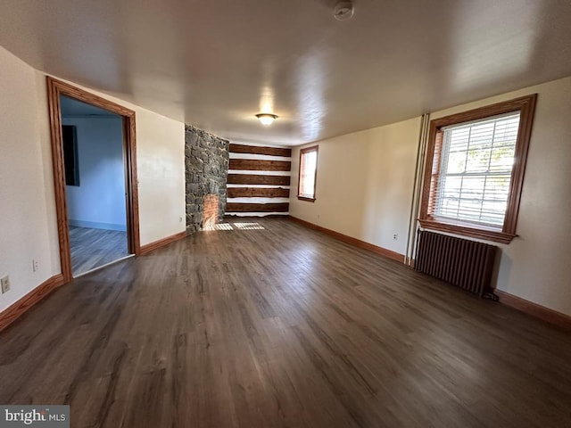 unfurnished living room featuring a stone fireplace, dark hardwood / wood-style floors, and radiator