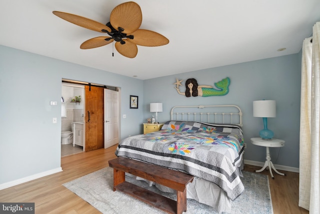 bedroom featuring a barn door, hardwood / wood-style flooring, ceiling fan, and ensuite bathroom