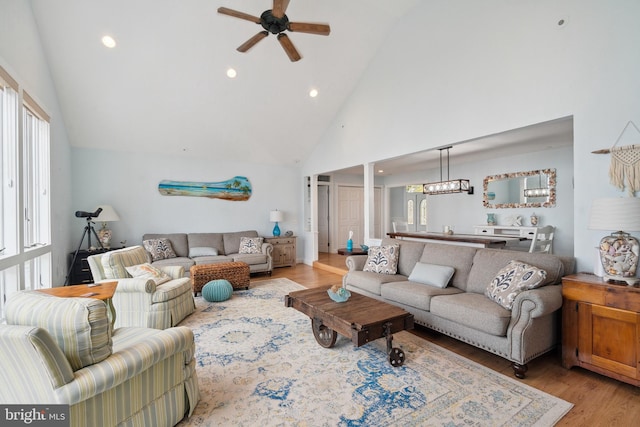 living room featuring high vaulted ceiling, ceiling fan with notable chandelier, light hardwood / wood-style floors, and plenty of natural light