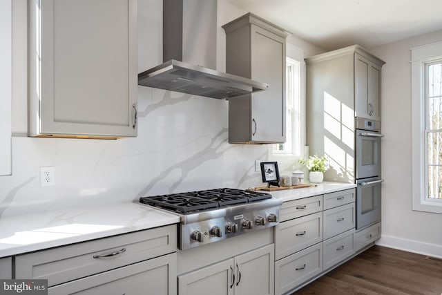 kitchen featuring gray cabinetry, stainless steel appliances, wall chimney range hood, decorative backsplash, and dark wood-type flooring