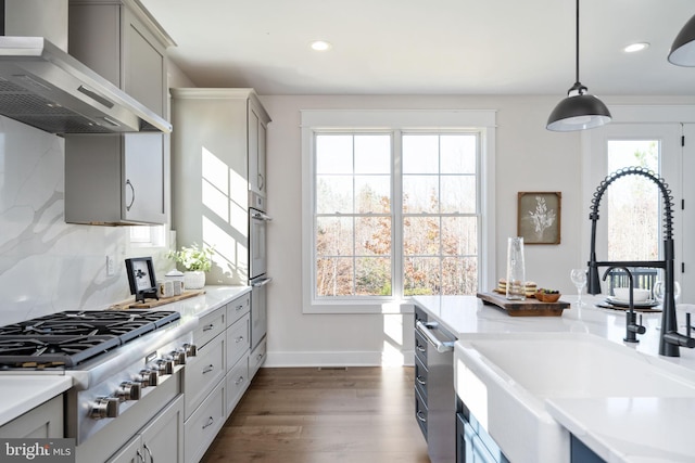 kitchen with stainless steel appliances, sink, gray cabinets, wall chimney range hood, and pendant lighting