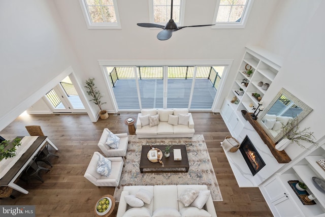 living room featuring dark wood-type flooring, a towering ceiling, ceiling fan, and a healthy amount of sunlight