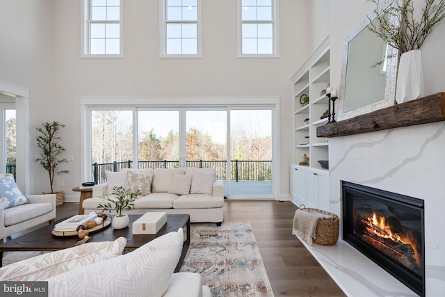 living room featuring dark hardwood / wood-style flooring, a high ceiling, built in features, and a premium fireplace