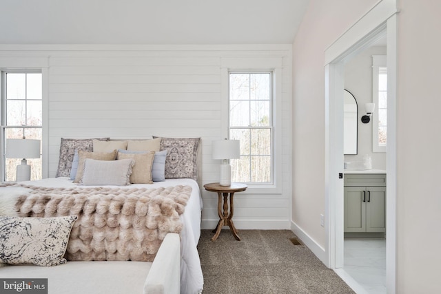 carpeted bedroom with multiple windows, wooden walls, and connected bathroom