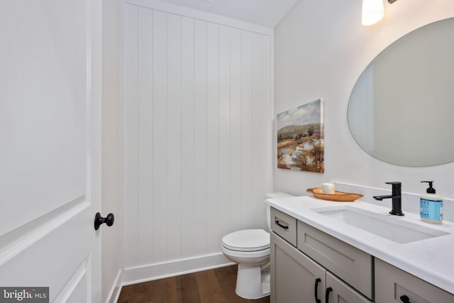 bathroom featuring wood-type flooring, wooden walls, toilet, and vanity