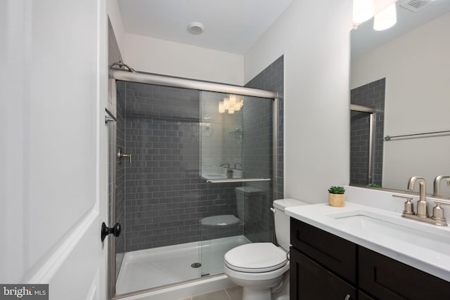 bathroom featuring toilet, vanity, tile patterned flooring, and a shower with shower door