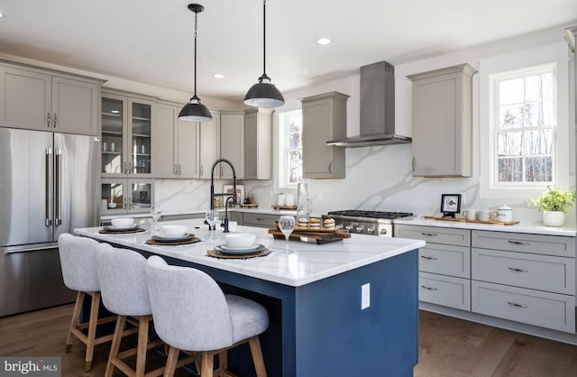 kitchen featuring appliances with stainless steel finishes, decorative light fixtures, dark hardwood / wood-style floors, an island with sink, and wall chimney exhaust hood