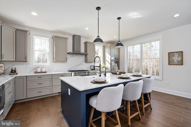 kitchen featuring dark hardwood / wood-style flooring, wall chimney range hood, a wealth of natural light, and a center island with sink